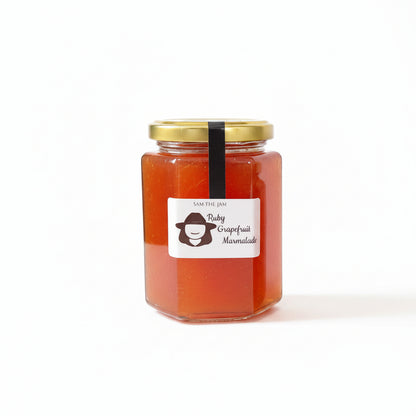 A glass jar of Sam the Jam Ruby Grapefruit Marzipanite jam with a gold lid and a white label featuring a cartoon character, set against a plain white background.